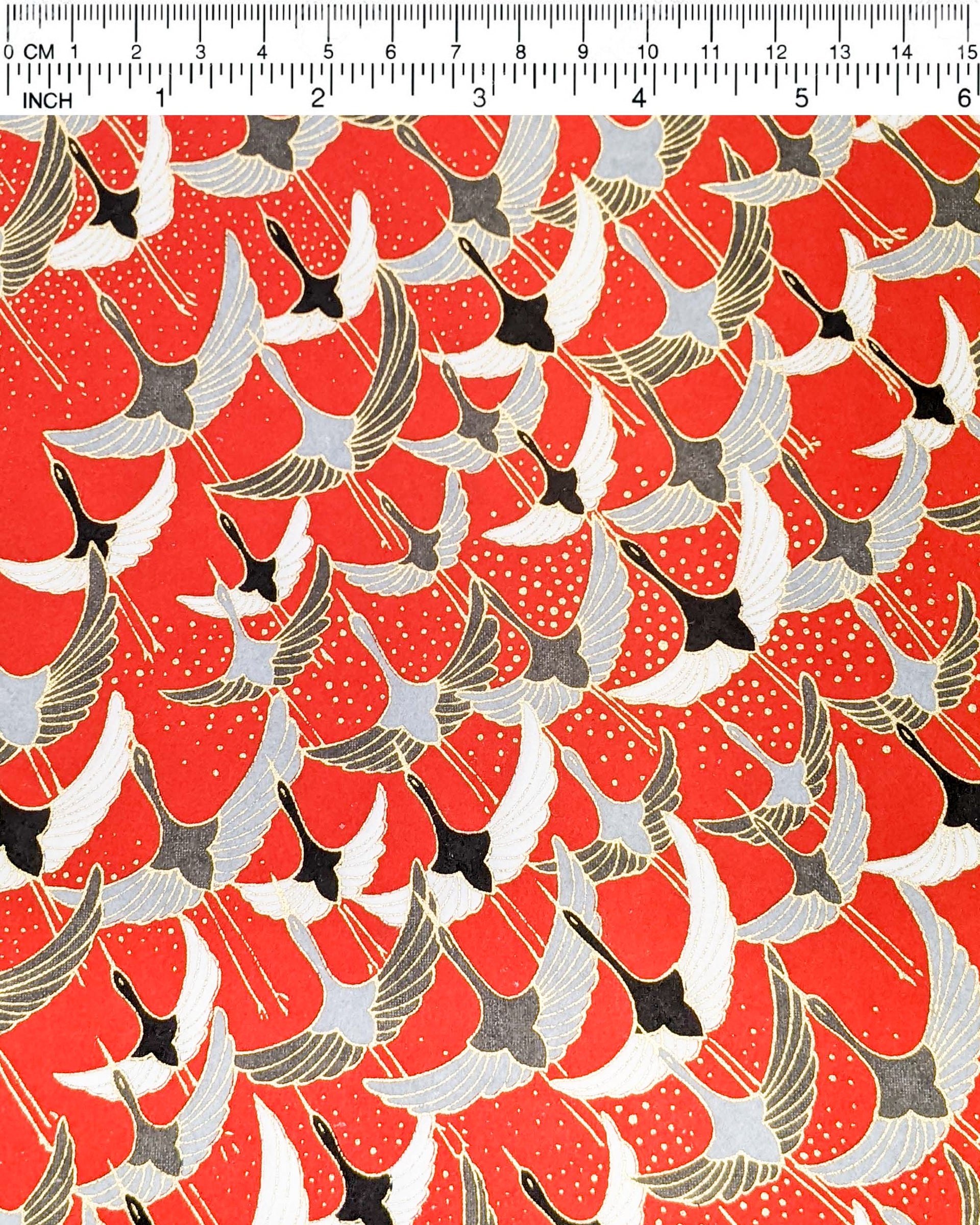 Japanese chiyogami paper featuring gray, black, and white flying cranes on a red background with metallic gold details. 