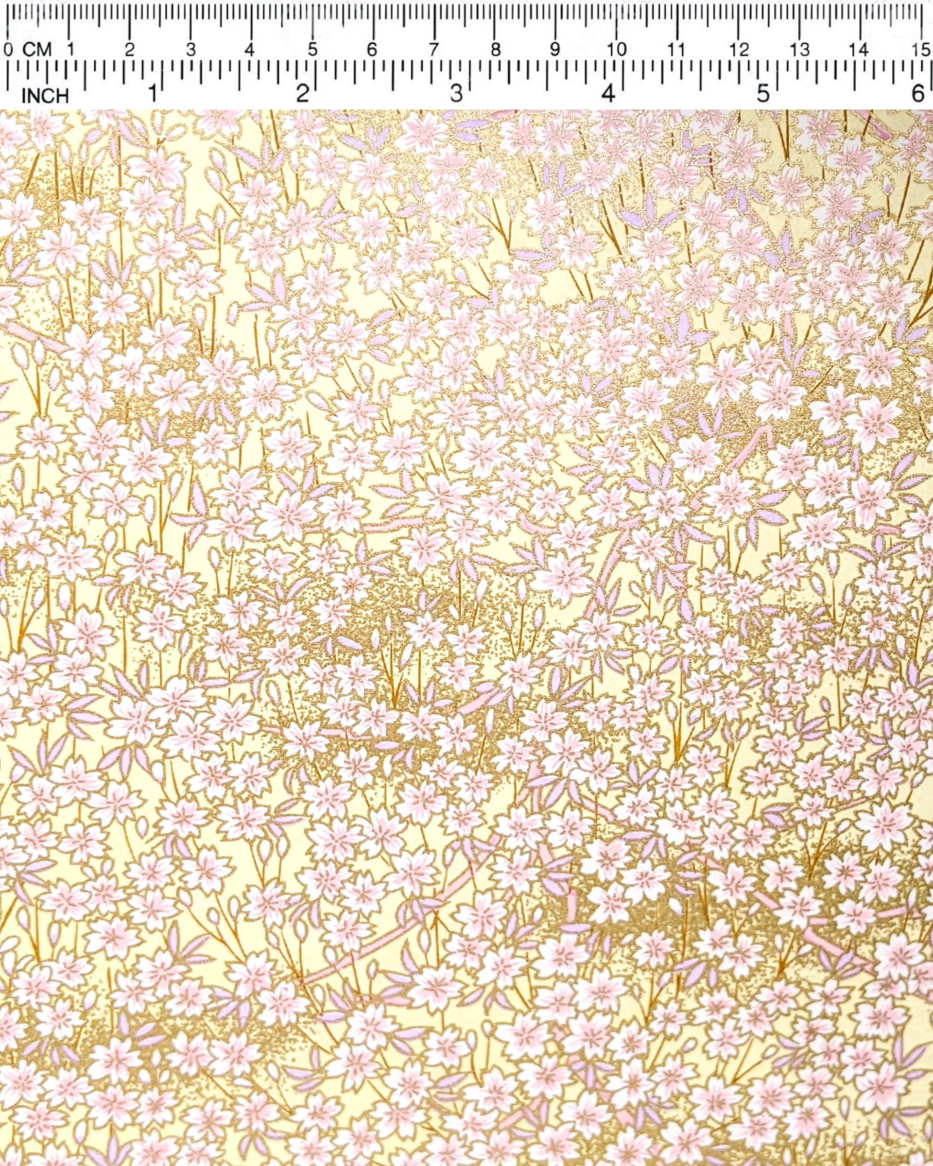 Japanese chiyogami paper featuring small white and light pink cherry blossoms on a yellow background with metallic gold details. 