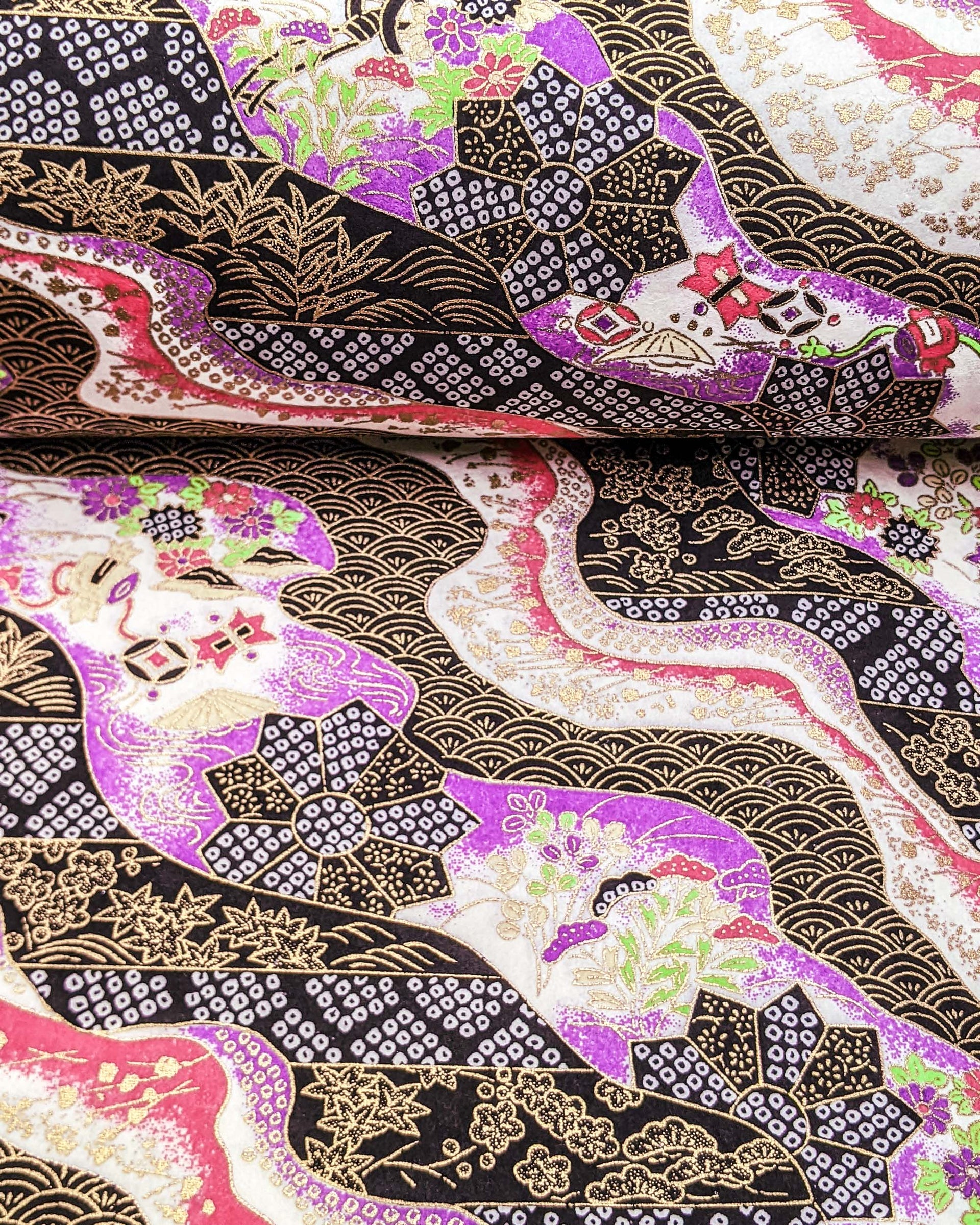 Japanese chiyogami paper featuring an assortment of purple, pink, and green flowers, flower cart motifs (hanaguruma), and traditional Japanese geometric designs with metallic gold details. The background is a mix of white, pink, purple, and black.