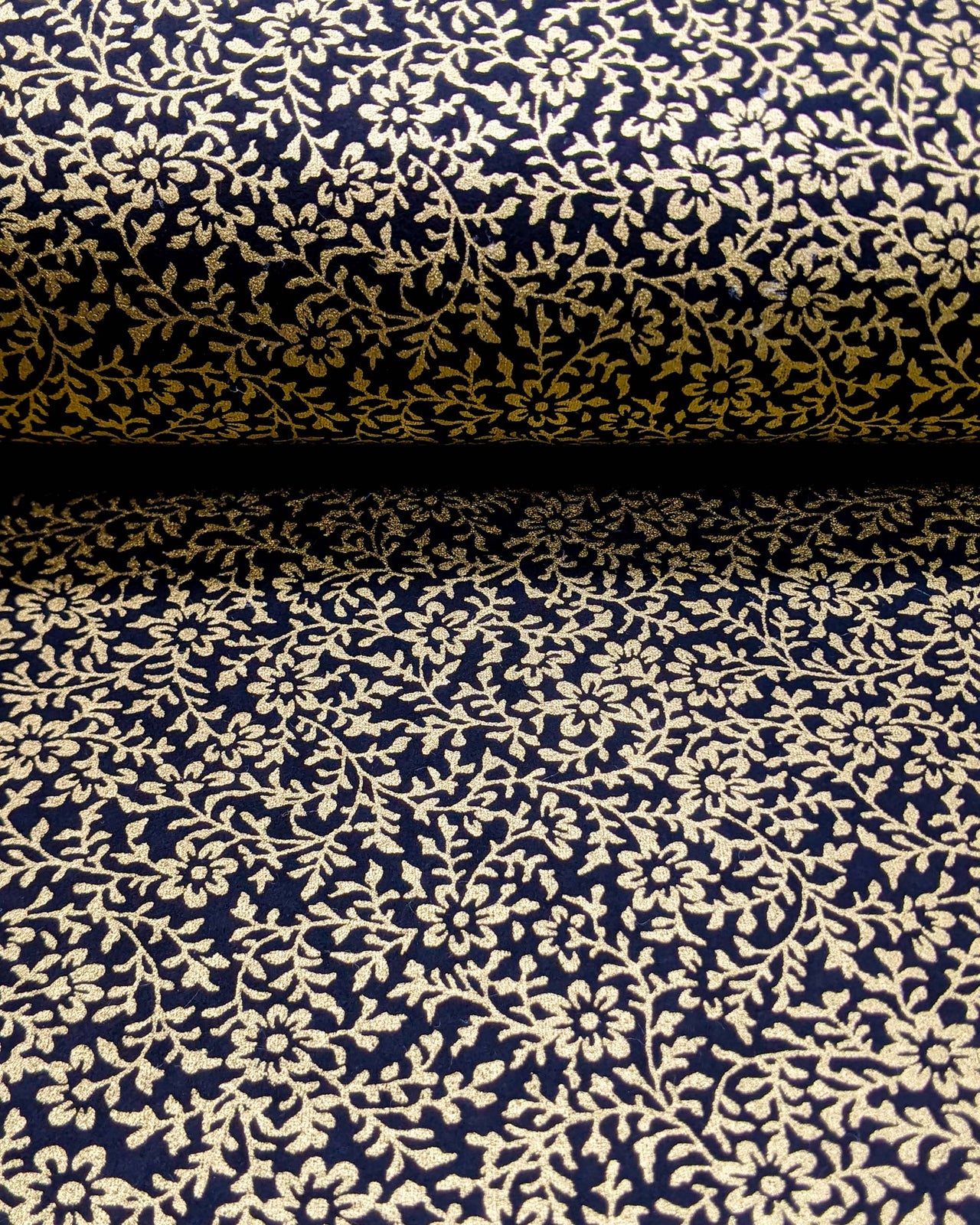 Japanese chiyogami paper featuring a metallic gold floral motif on a black background, shown rolled to highlight the design.