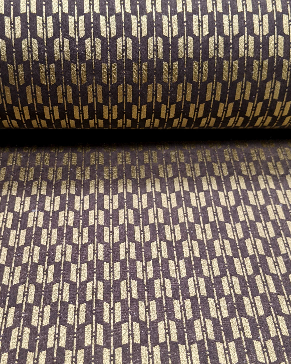 Japanese chiyogami paper featuring a traditional metallic gold yagasuri (arrow fletching) pattern on a gray background, shown rolled to highlight the design.