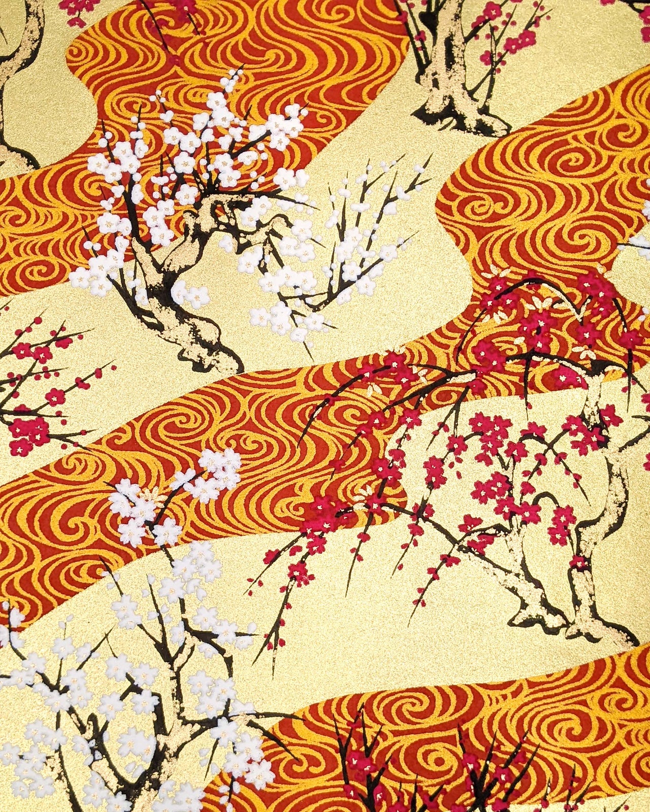 Japanese chiyogami paper featuring pink and white plum and cherry blossom trees set against a metallic gold and red water ripple pattern on a gold background.
