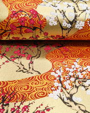 Japanese chiyogami paper featuring pink and white plum and cherry blossom trees set against a metallic gold and red water ripple pattern on a gold background, shown rolled to highlight the design.