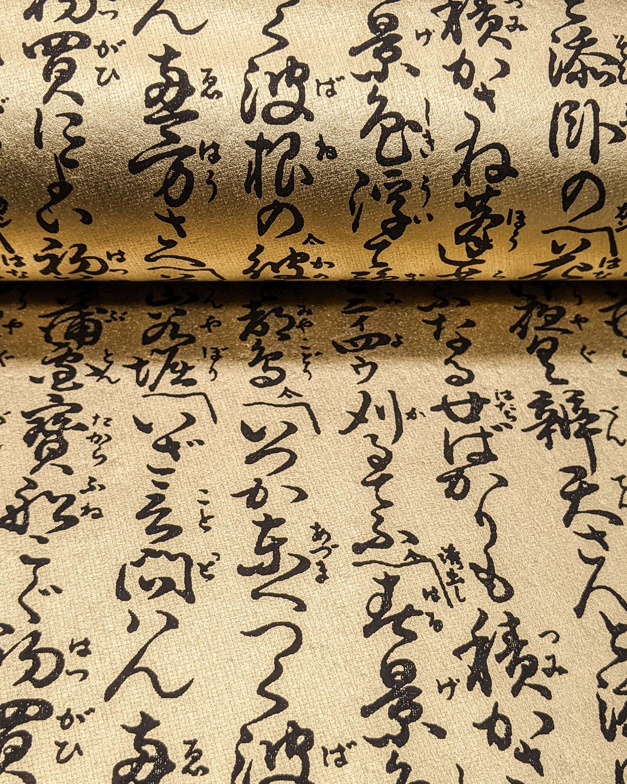 Japanese chiyogami paper featuring black Japanese calligraphy on a metallic gold background, shown rolled to highlight the design.