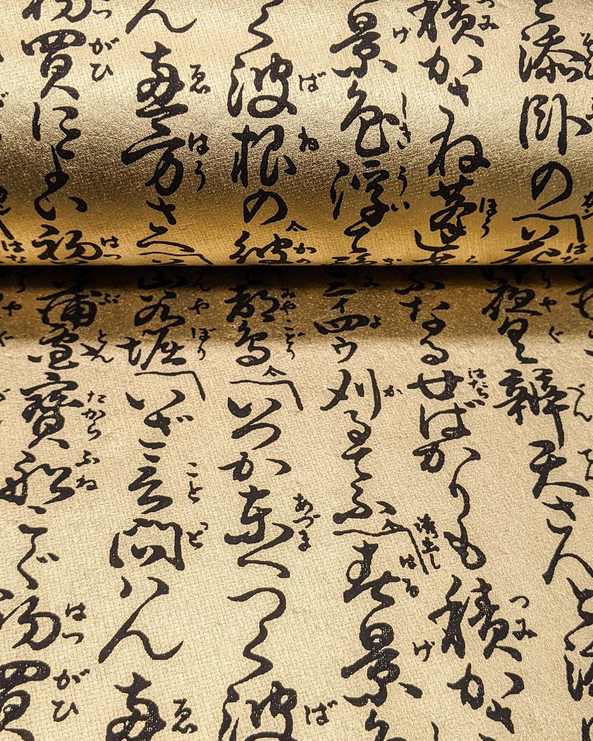 Japanese chiyogami paper featuring black Japanese calligraphy on a metallic gold background, shown rolled to highlight the design.