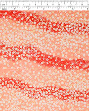 Japanese chiyogami paper featuring small white and metallic gold cherry blossoms on a gradient red background, shown next to a ruler for size reference.