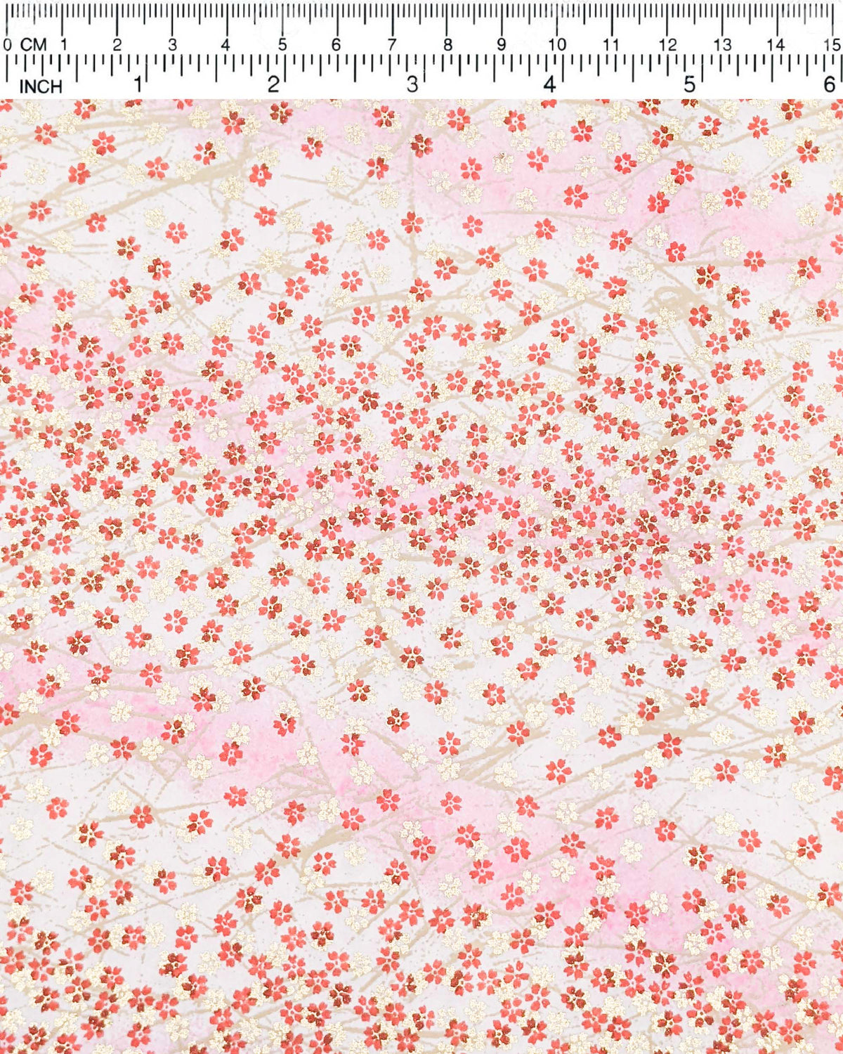 Japanese chiyogami paper featuring small red and metallic gold cherry blossoms on a gradient light pink background, shown next to a ruler for size reference.