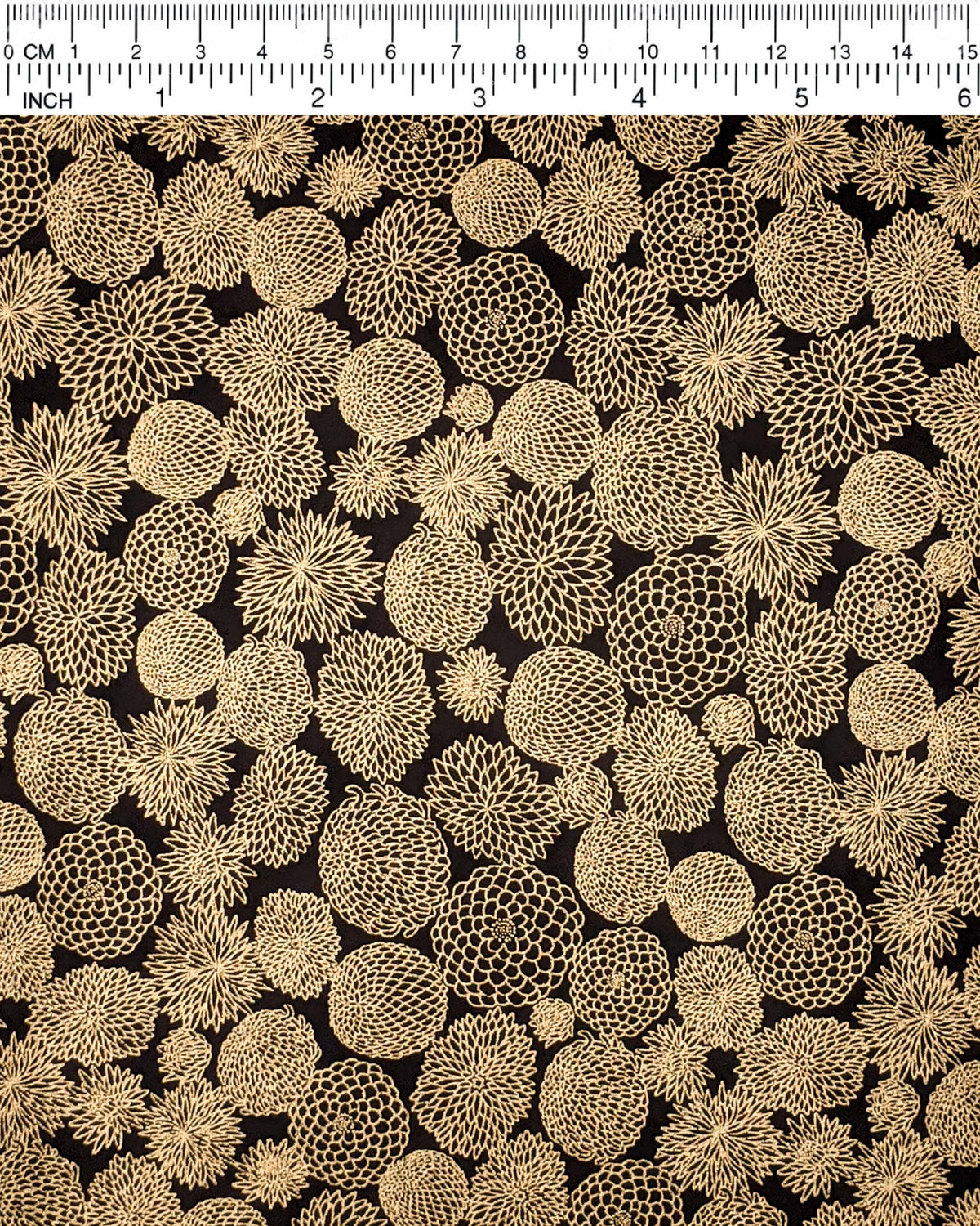 Japanese chiyogami paper featuring an assortment of small metallic gold chrysanthemums on a black background, shown next to a ruler for size reference.