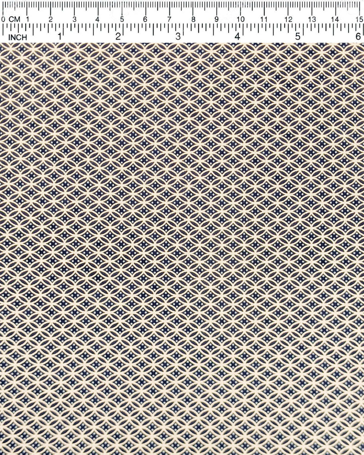 Japanese chiyogami paper featuring a traditional oval shippo pattern in metallic gold with four white dots in the center on a black background, shown next to a ruler for size reference.
