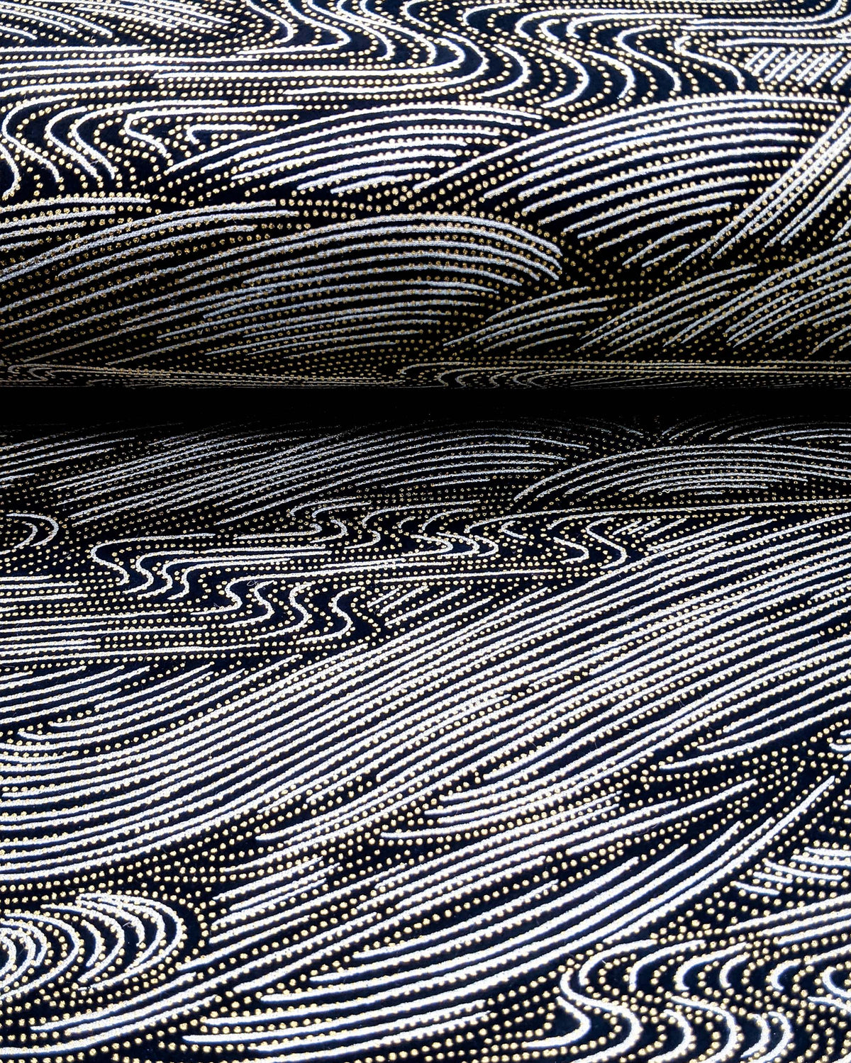 Japanese chiyogami paper featuring flowing metallic silver ripples with metallic gold dotted details on a black background, shown rolled to highlight the design.