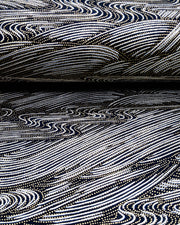 Japanese chiyogami paper featuring flowing metallic silver ripples with metallic gold dotted details on a black background, shown rolled to highlight the design.