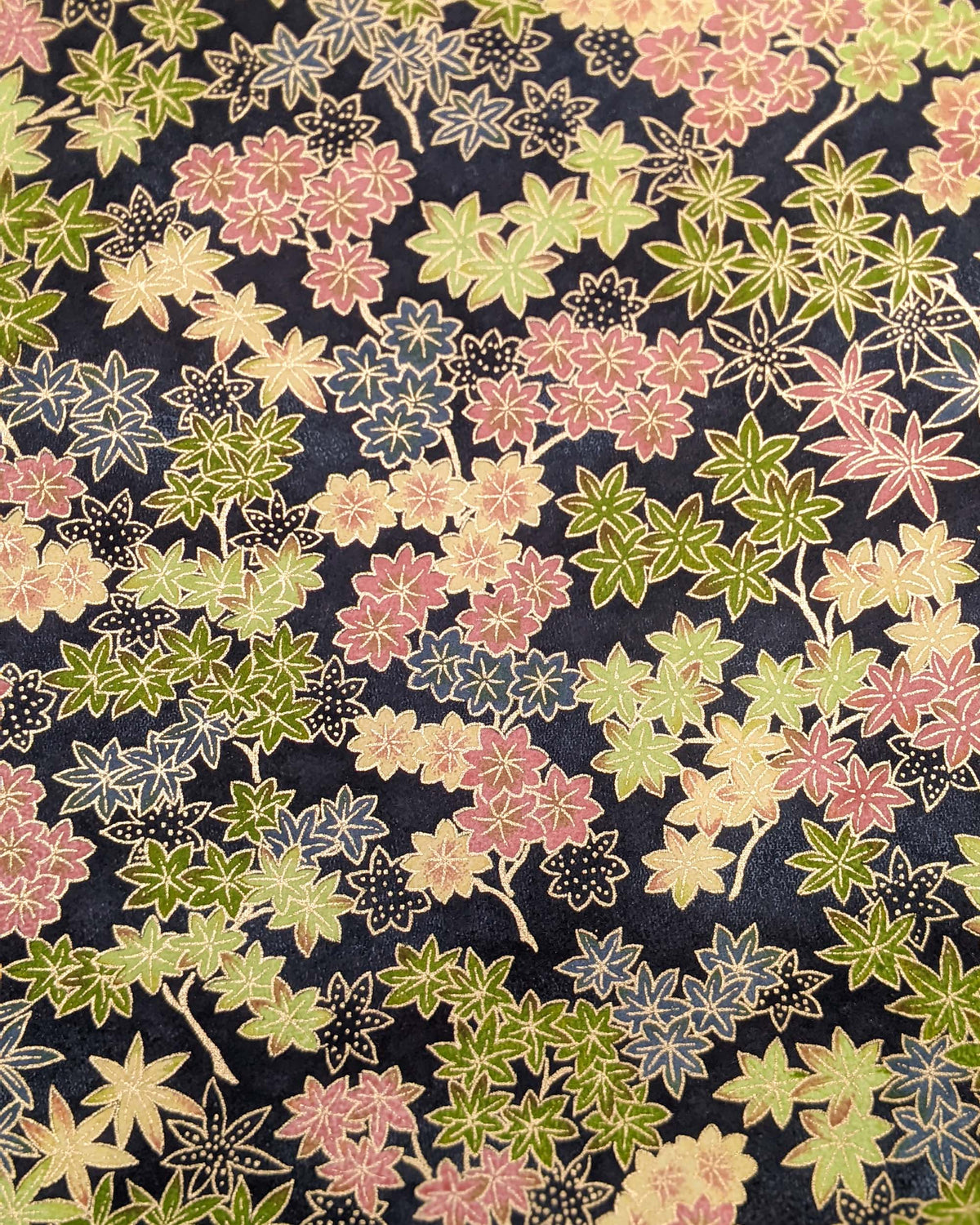 Japanese chiyogami paper featuring assorted green, pink, beige, and gray maple leaves with dark gray and metallic gold dotted maple leaves on a dark gray background.