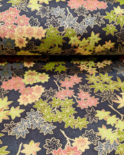 Japanese chiyogami paper featuring assorted green, pink, beige, and gray maple leaves with dark gray and metallic gold dotted maple leaves on a dark gray background, shown rolled to highlight the design.
