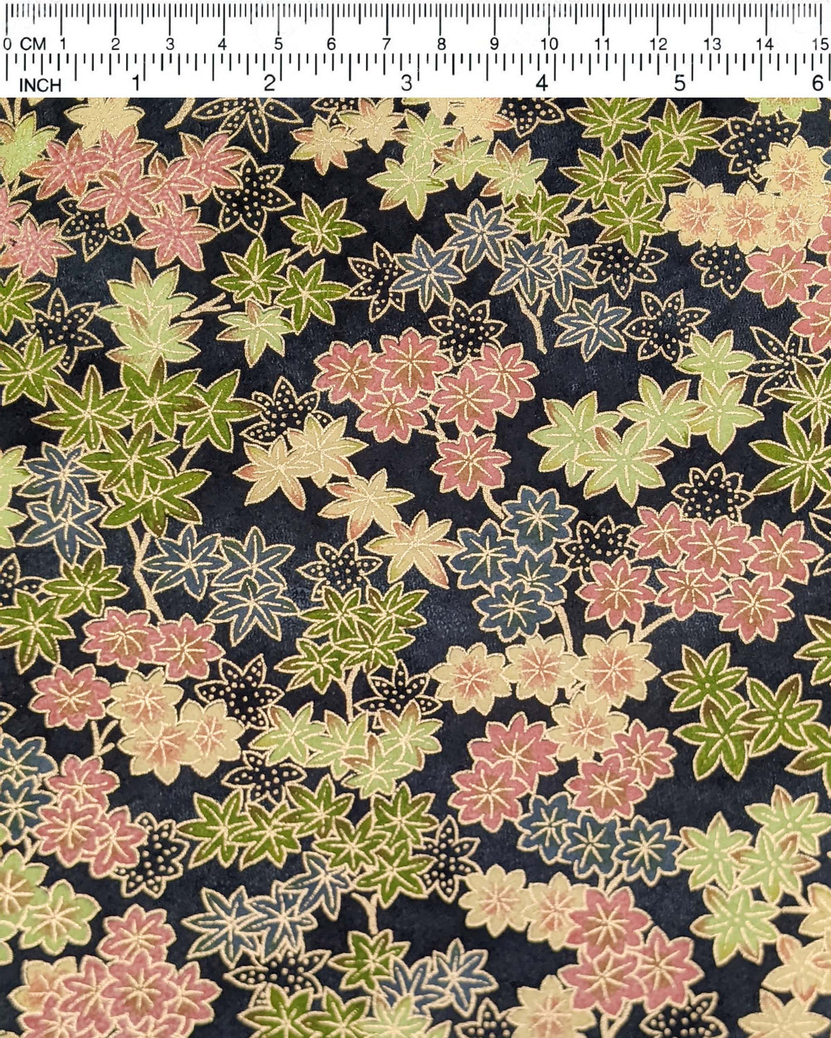 Japanese chiyogami paper featuring assorted green, pink, beige, and gray maple leaves with dark gray and metallic gold dotted maple leaves on a dark gray background, shown next to a ruler for size reference.