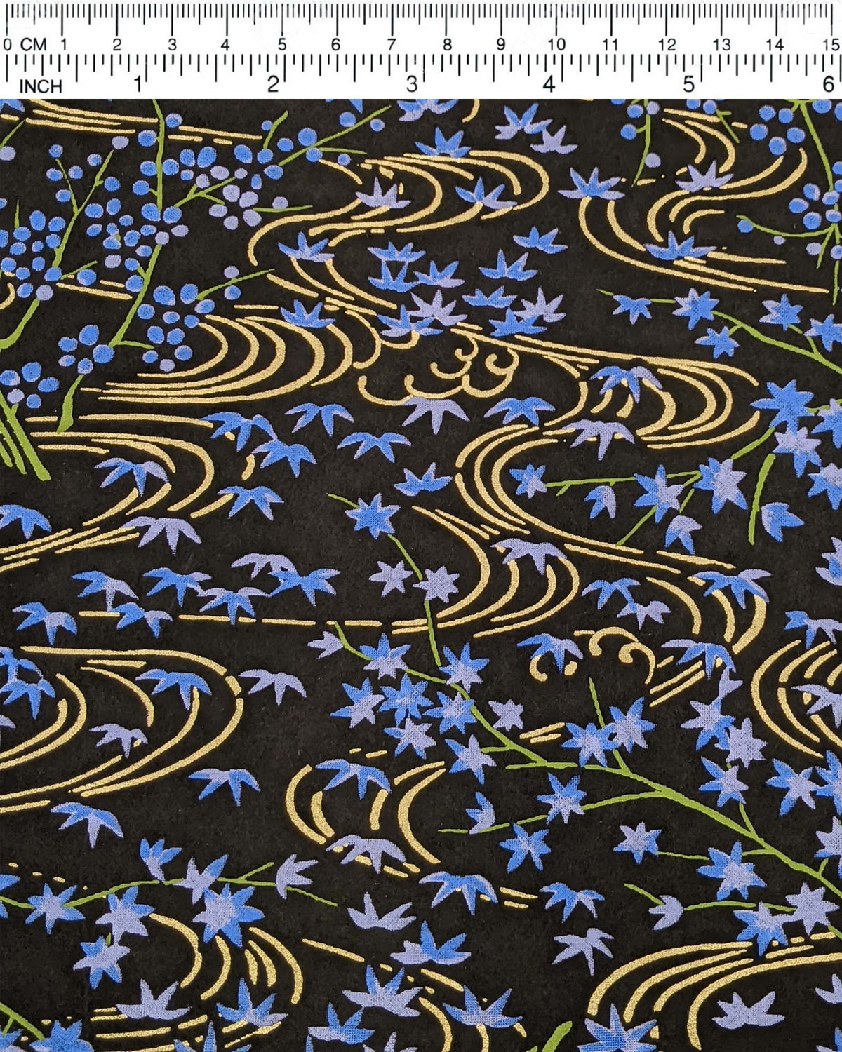 Japanese chiyogami paper featuring small blue maples leaves with green branches over flowing metallic gold streams on a black background, shown next to a ruler for size reference.