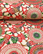 Japanese chiyogami paper featuring large red and green zinnia flowers on a cream background, shown rolled to highlight the design.