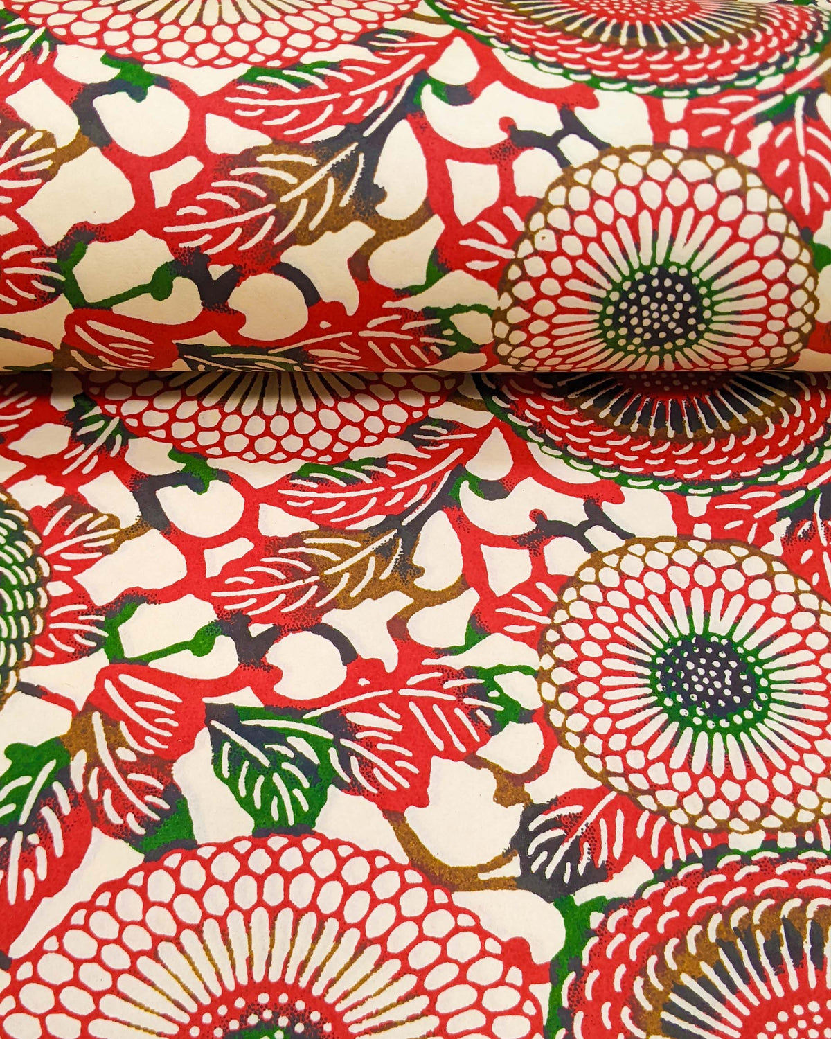 Japanese chiyogami paper featuring large red and green zinnia flowers on a cream background, shown rolled to highlight the design.
