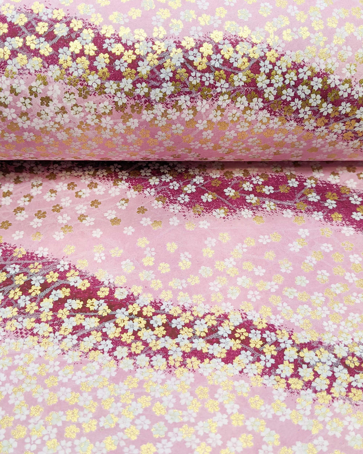 Japanese chiyogami paper featuring small white and metallic gold cherry blossoms on a gradient purple background, shown rolled to highlight the design.