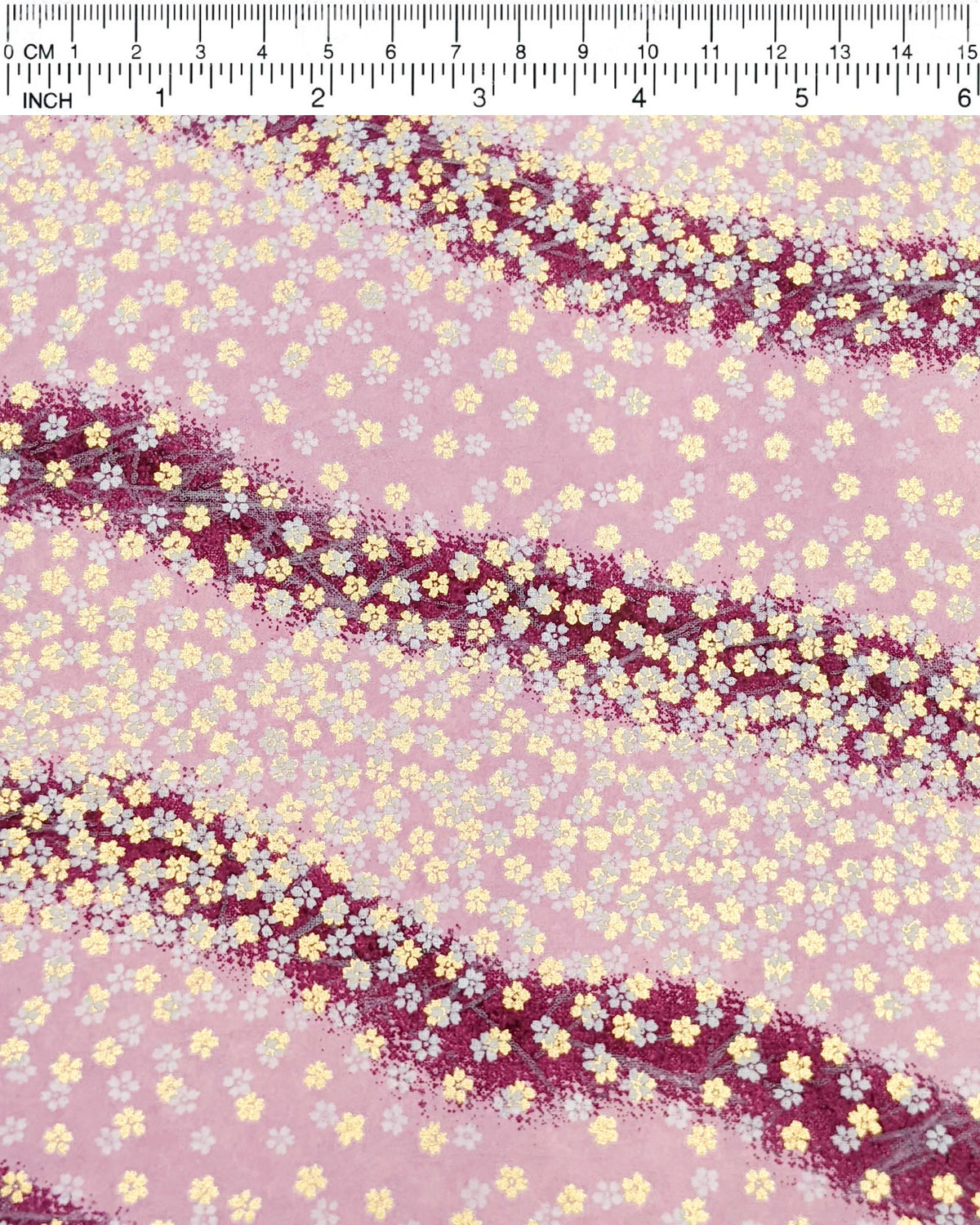 Japanese chiyogami paper featuring small white and metallic gold cherry blossoms on a gradient purple background, shown next to a ruler for size reference.