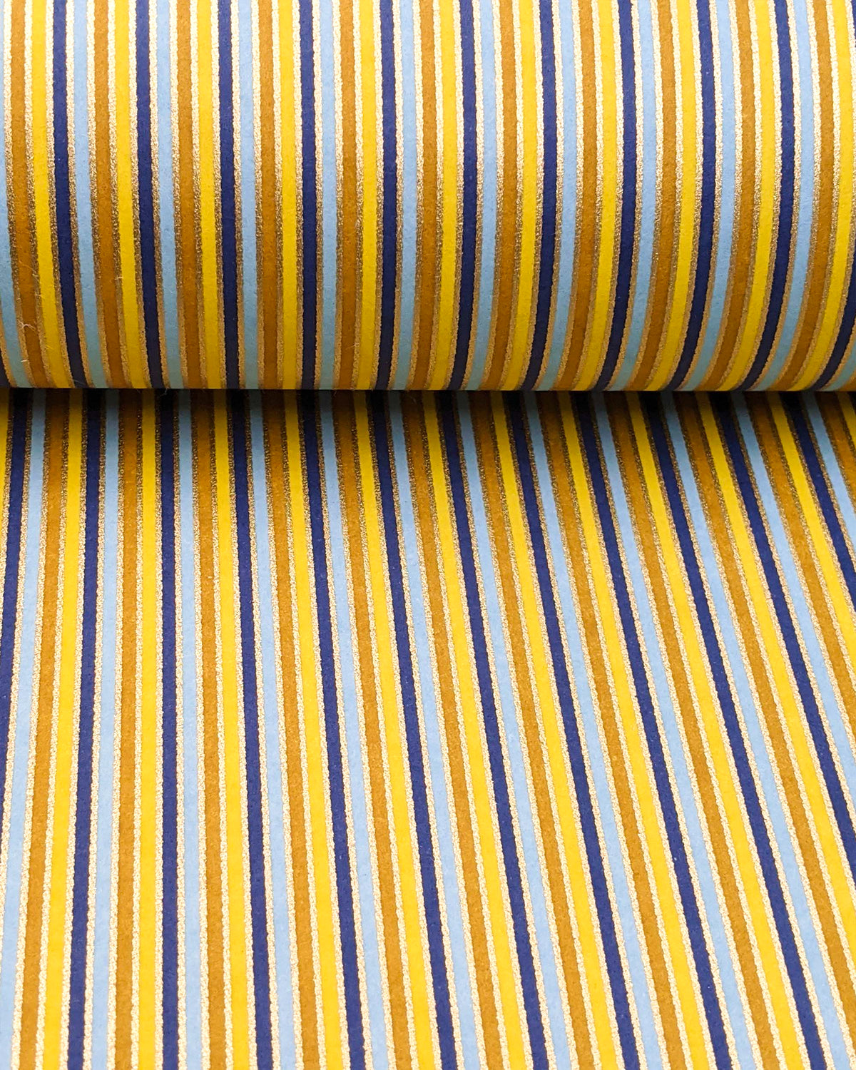 Japanese chiyogami paper featuring vertical stripes in light and golden yellow, light blue, and dark blue with metallic gold stripes, shown rolled to highlight the design.