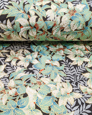 Japanese chiyogami paper featuring green and white leaves with metallic silver leaves on a black background with metallic gold details, shown rolled to highlight the design.