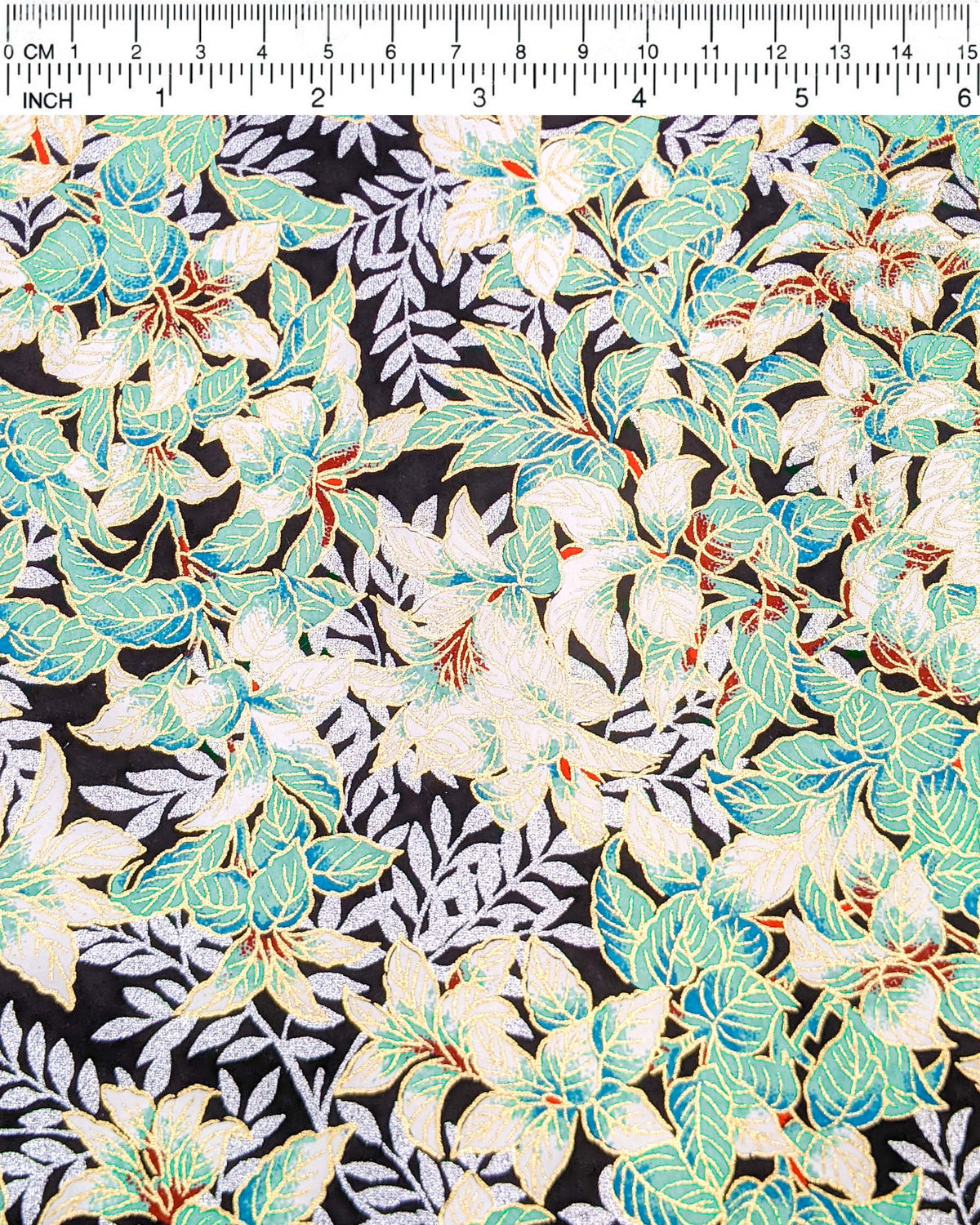 Japanese chiyogami paper featuring green and white leaves with metallic silver leaves on a black background with metallic gold details, shown next to a ruler for size reference.
