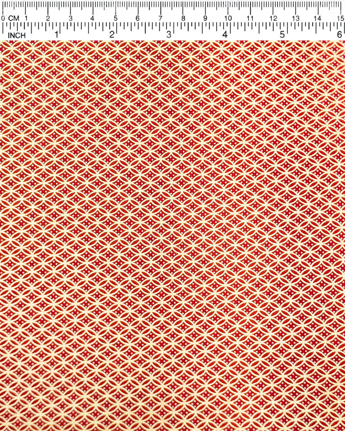 Japanese chiyogami paper featuring a traditional oval shippo pattern in metallic gold with four white dots in the center on a red background, shown next to a ruler for size reference.