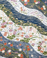 Japanese chiyogami paper featuring red, purple, pink, and white chrysanthemums, plum blossoms, wisteria, and other flowers arranged among traditional Japanese patterns on a blue and silver background with metallic gold details.
