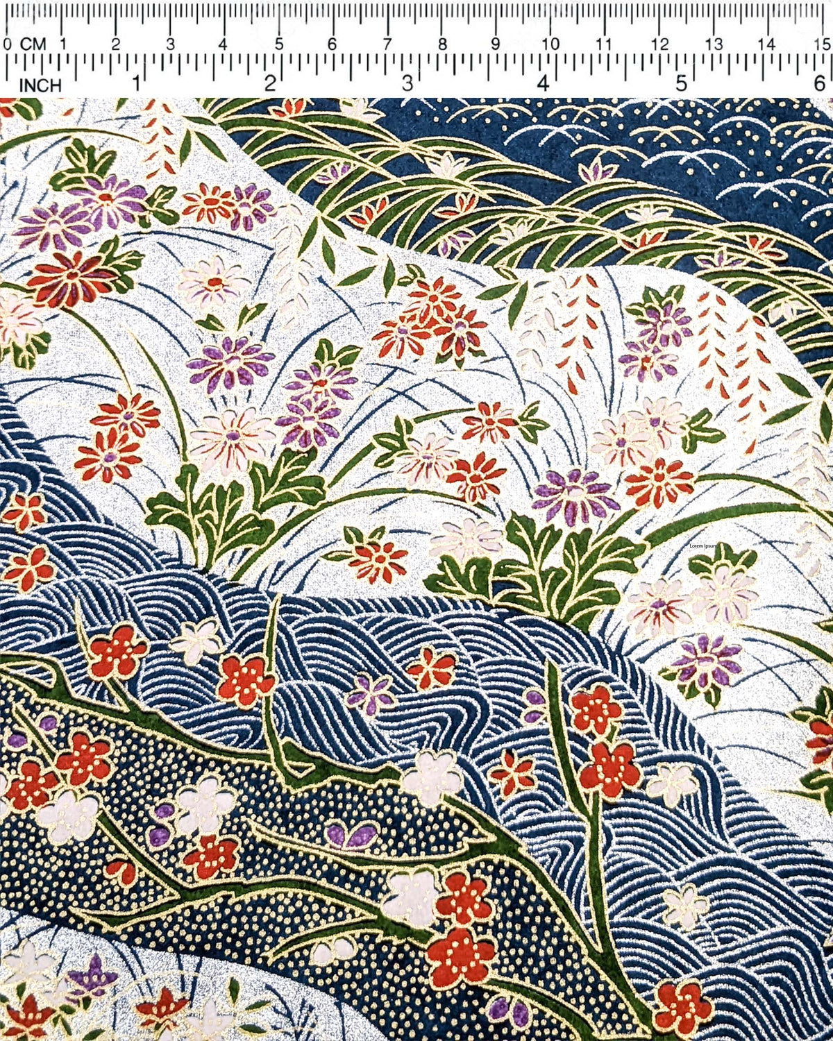 Japanese chiyogami paper featuring red, purple, pink, and white chrysanthemums, plum blossoms, wisteria, and other flowers arranged among traditional Japanese patterns on a blue and silver background with metallic gold details, shown next to a ruler for size reference.